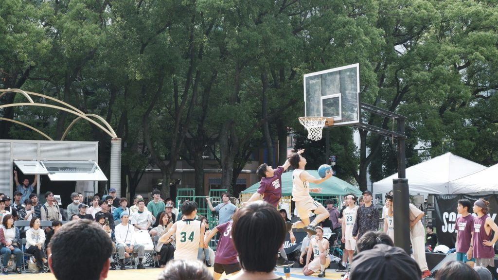 Basketball players competing in an outdoor game with spectators watching