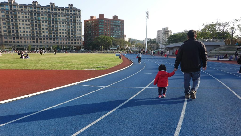 Man and child walking on a blue running track.